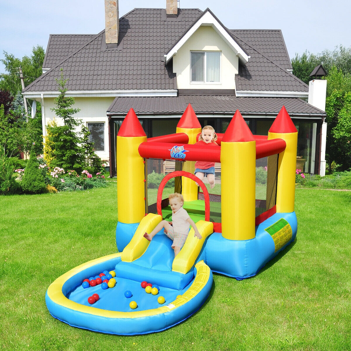 Inflatable bounce house with slide and ball pit on grass lawn, kids playing outside